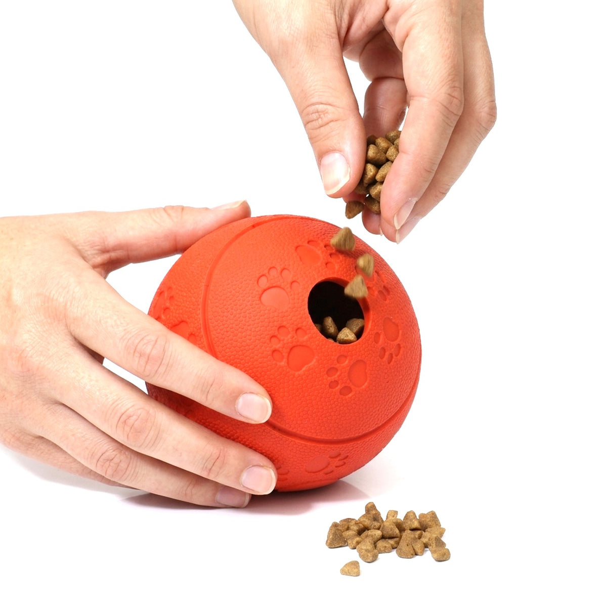 Hands filling the red treat dispensing dog ball with dry kibble through the round opening