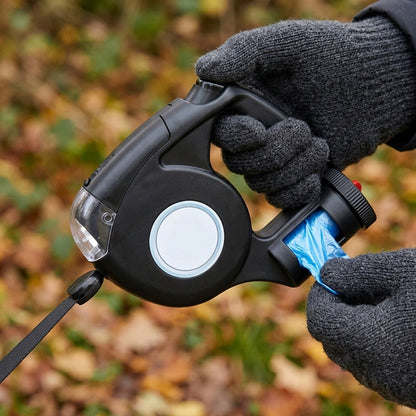 Gloved hand pulling a poo bag from the holder under the handle of a black retractable dog lead